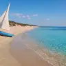 Barca a vela sulla sabbia bianca di Punta Prosciutto, con le dune e il mare chiaro