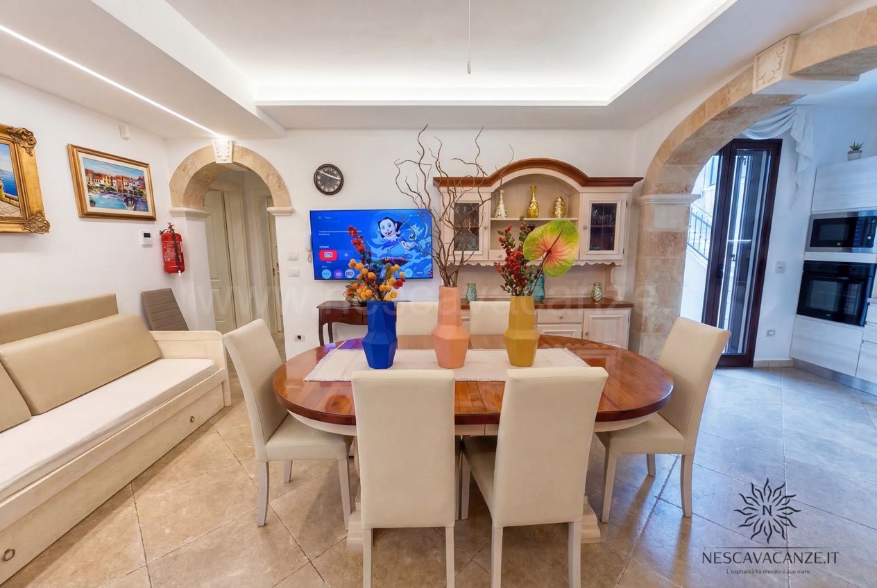 Casa Pescoluse 9 - soggiorno con tavolo ovale in legno, sedie color crema, divano, TV e archi in pietra
