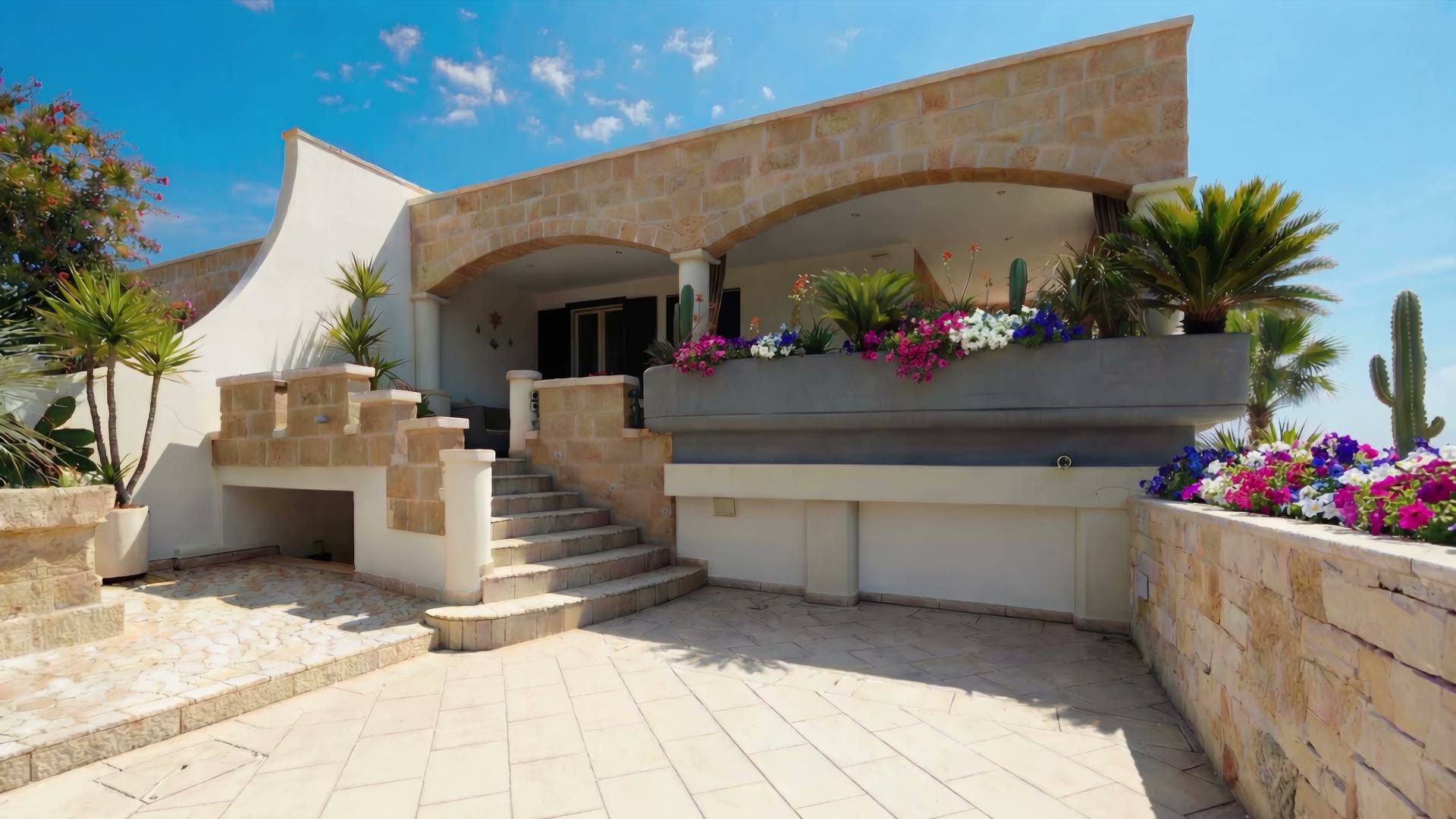 Il cortile pavimentato di Casa Pescoluse 1 con le fioriere fiorite, la scala in pietra e la veranda ad archi