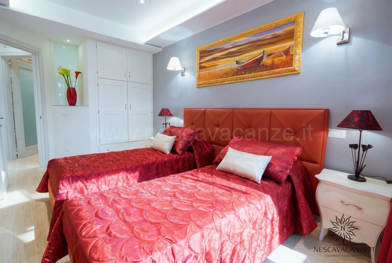 Casa Salento - camera doppia con letti rossi, armadio bianco e quadro con barca sulla parete grigia