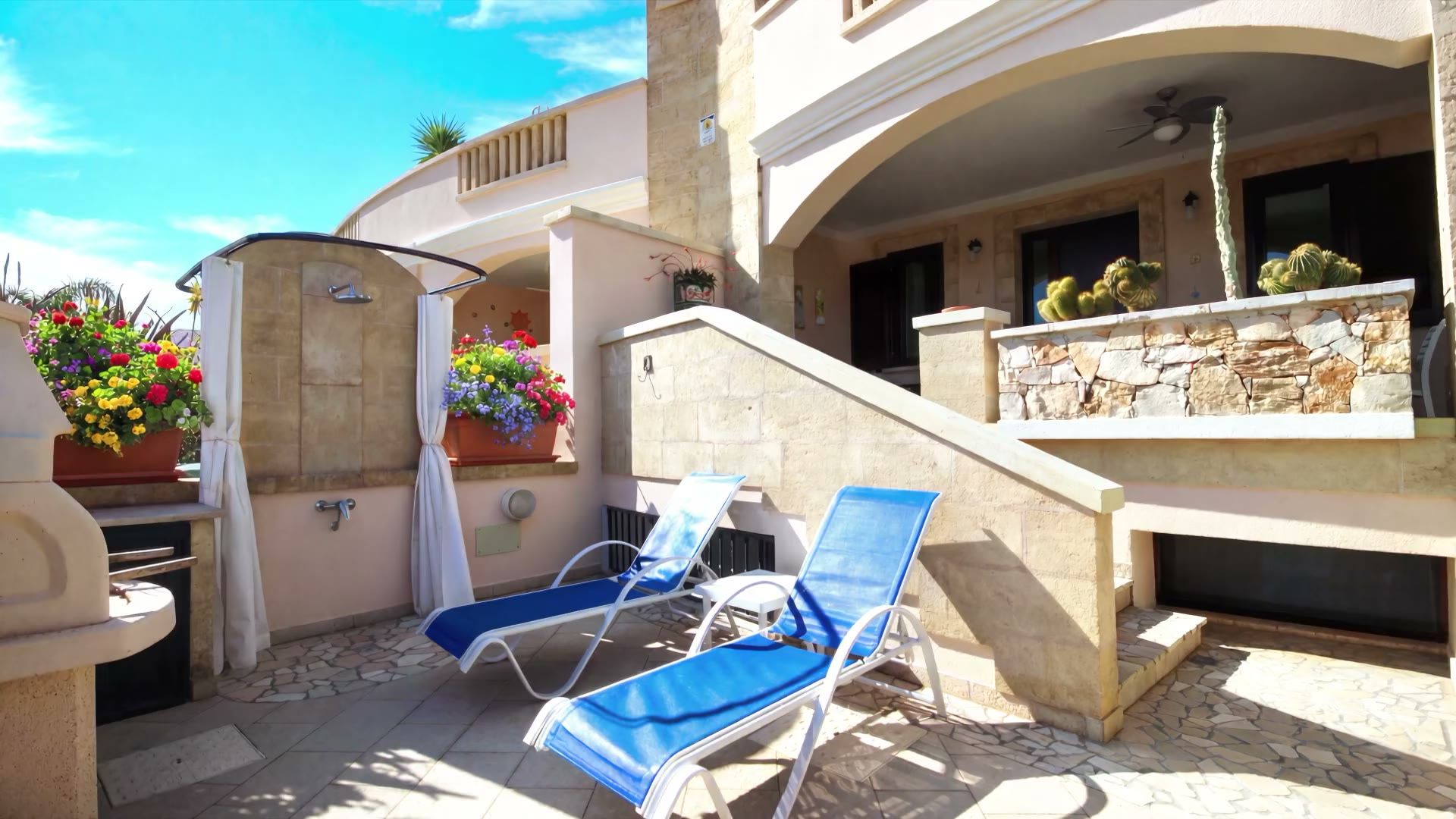 Il cortile pavimentato di Casa Pescoluse 5 con i due lettini blu, la doccia esterna con le tende e la scala in pietra