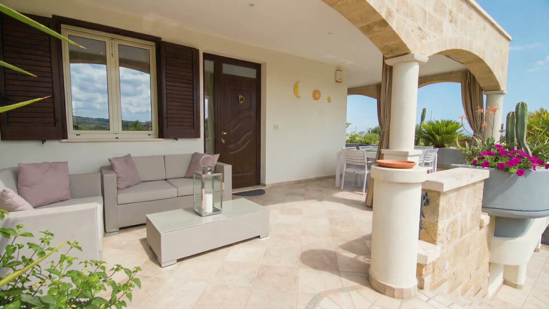 La veranda coperta di Casa Pescoluse 1 con i divani, i cuscini rosa antico, la lanterna e il tavolino basso