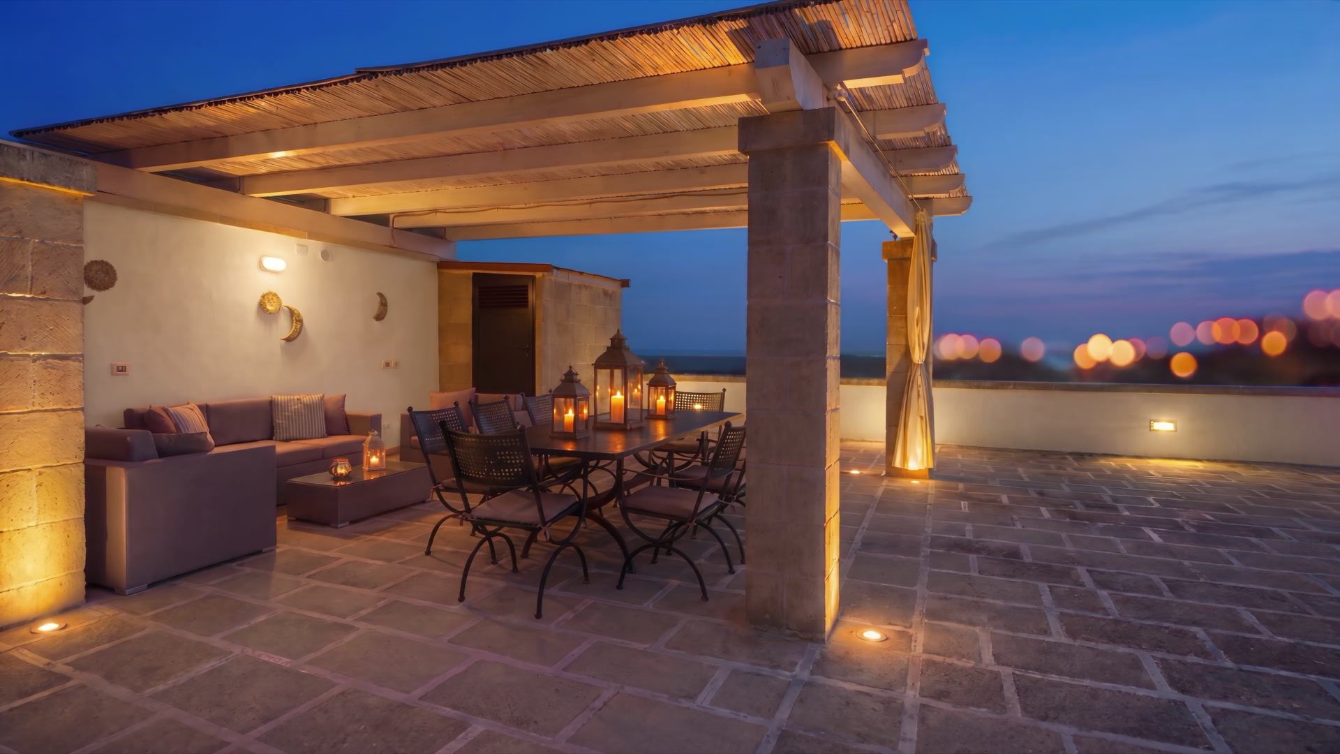 Terrazza illuminata di Casa Pescoluse 4 al crepuscolo, con le tende mosse dal vento