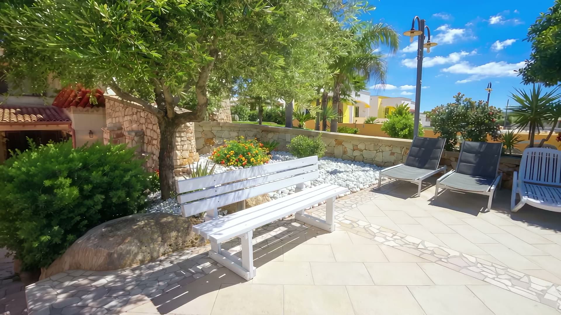 Il giardino d'ingresso di Casa Pescoluse 9: la panca bianca, il muretto a secco con i fiori, i lettini prendisole, l'ulivo e le palme