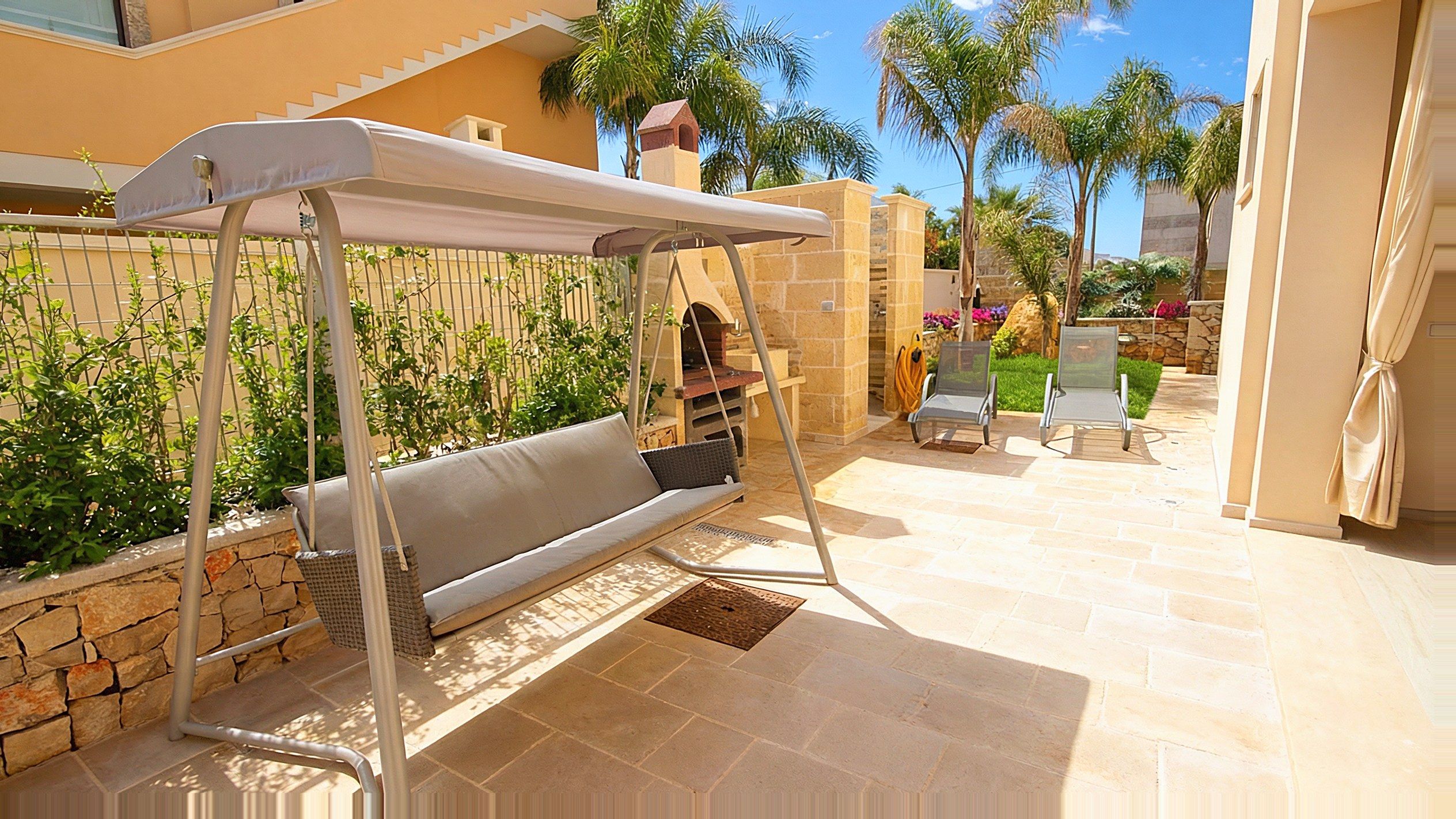 Il giardino interno di Casa Salento a Pescoluse: il dondolo, il barbecue a legna in muratura, i lettini prendisole sul prato inglese e le palme