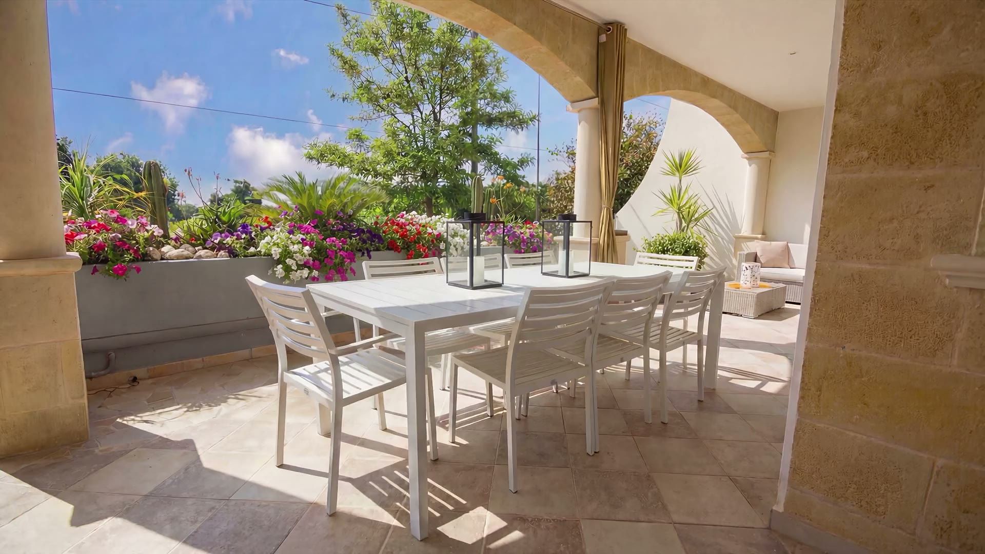 Il tavolo da pranzo bianco con otto sedie sulla veranda di Casa Pescoluse 1, fra le fioriere fiorite e gli archi in travertino