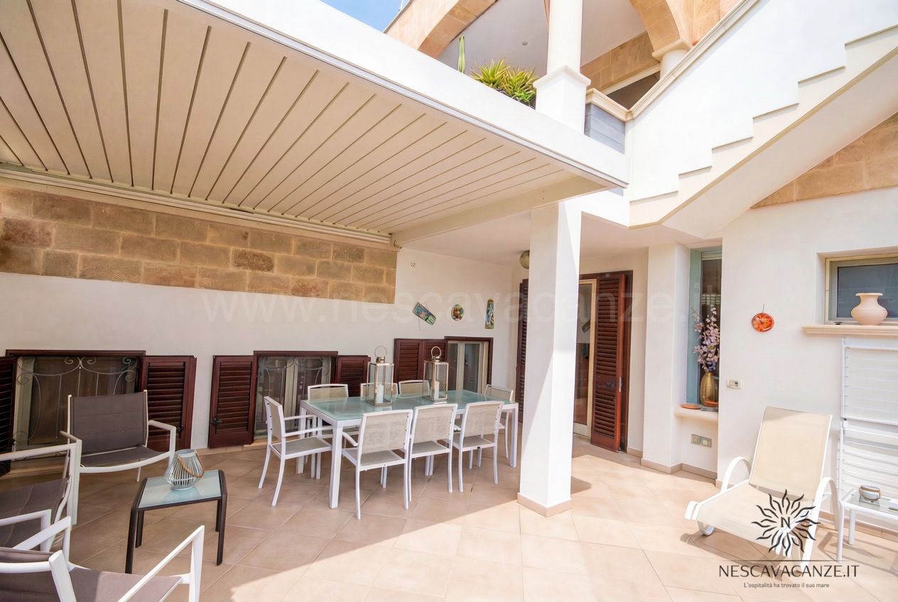 Casa Pescoluse 2 - veranda coperta con tavolo da pranzo, sedie bianche e lanterne