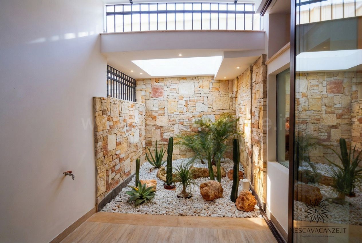 Casa Salento - cavedio interno con giardino di cactus e palme su ghiaia bianca e parete in pietra