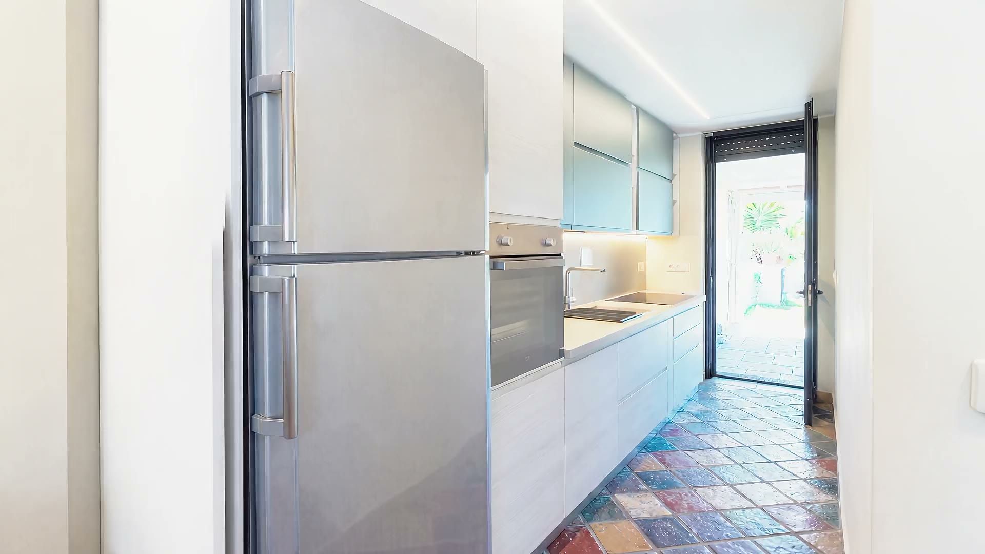 La cucina di Casa Sabbia d'Oro: il frigorifero, il forno e il piano di lavoro lungo il corridoio che esce sul giardino