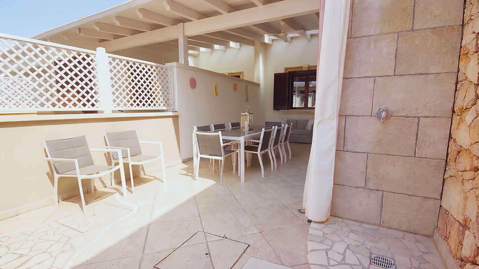La veranda di Casa Pescoluse 9 sotto le travi bianche: le poltroncine, il tavolo da pranzo esterno da otto e la doccia esterna in pietra