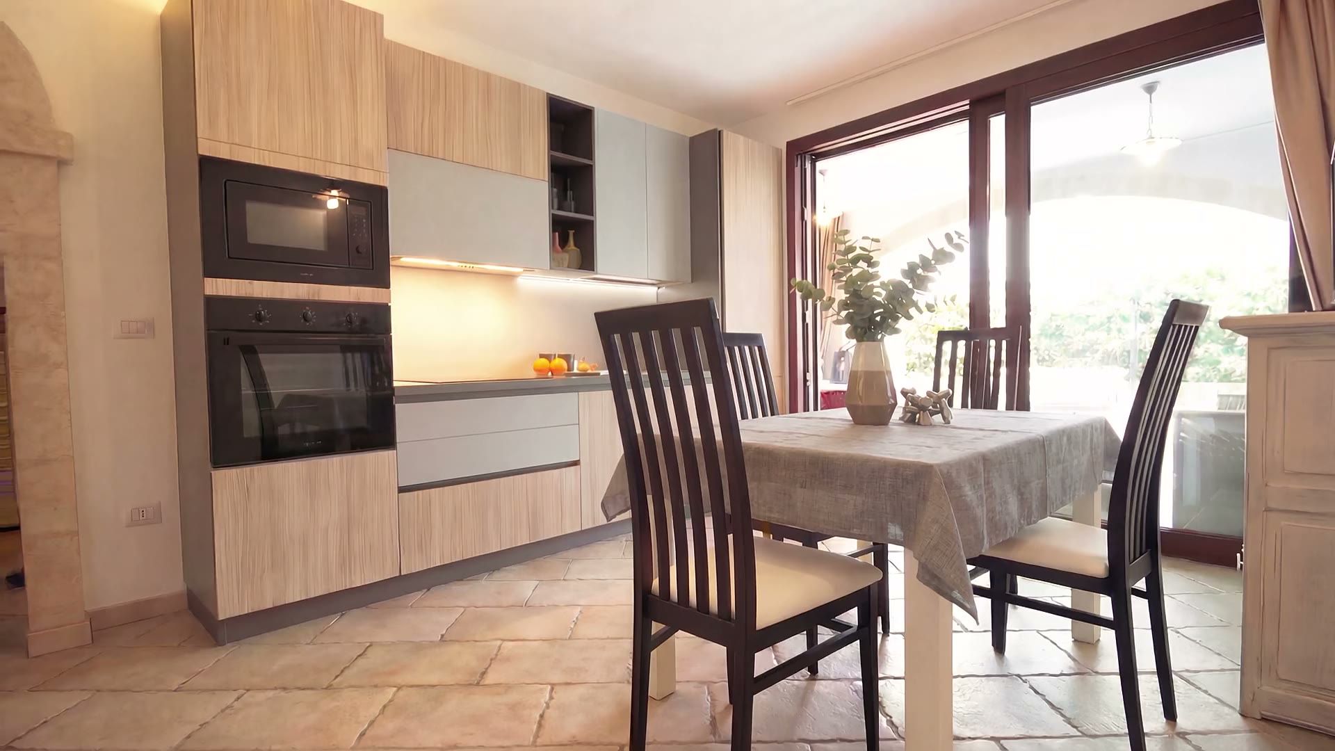 Il soggiorno di Casa Pescoluse 6 con il pavimento in cotto, il tavolo da pranzo, il divano e la cucina in legno e grigio sullo sfondo