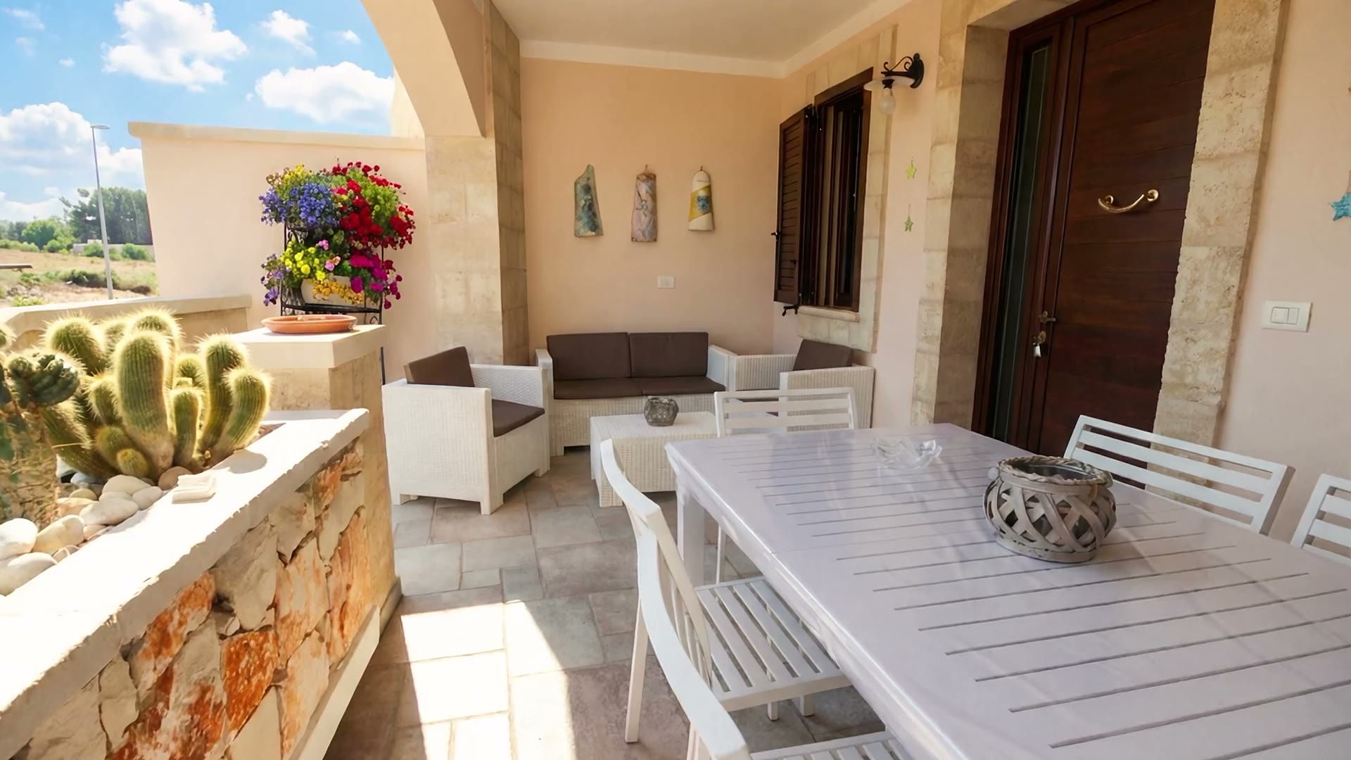 Il salottino in rattan sulla veranda di Casa Pescoluse 5, con il tavolo bianco e la porta d’ingresso in legno scuro