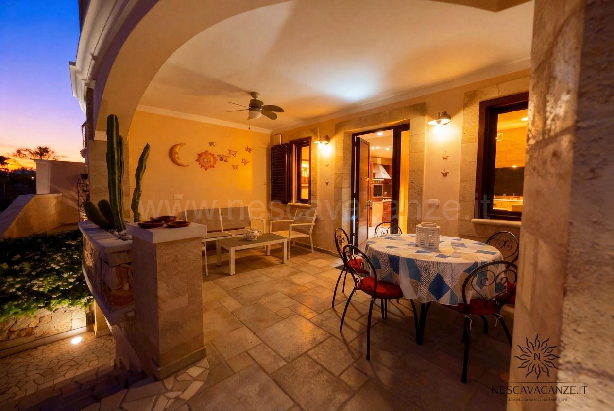 Casa Pescoluse 4 - veranda al tramonto con tavolo tondo, sedie in ferro rosse, divanetto e cactus