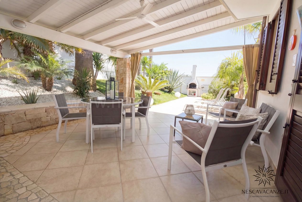 Casa Pescoluse 3 - veranda coperta con tavolo da pranzo in vetro, poltrone imbottite e affaccio sul giardino