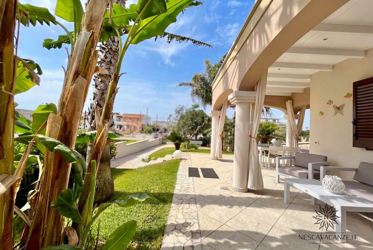 Casa Pescoluse 8 - Veranda laterale con divano, tavolino e piante di banano, giardino sul lato
