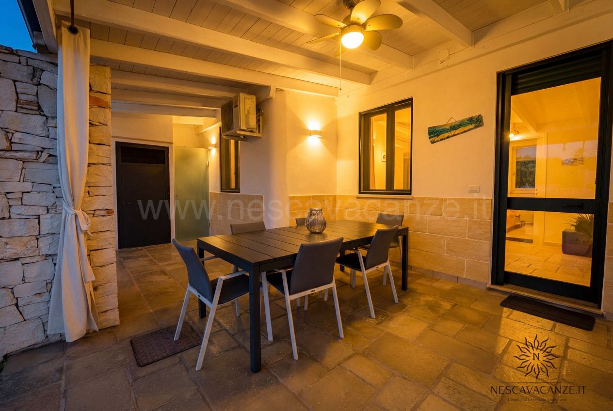 Casa Sabbia Oro - veranda serale con tavolo, sedie, ventilatore acceso e porta-finestra illuminata