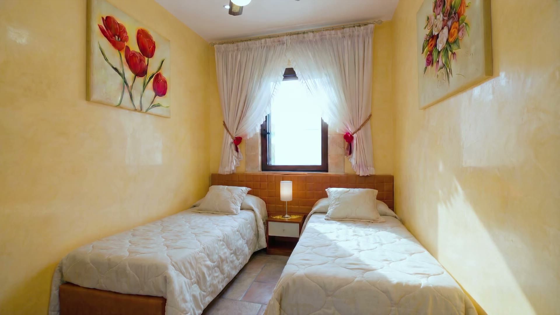 La seconda camera di Casa Pescoluse 5 con i due letti singoli, la finestra ad arco con le tende bianche e i quadri floreali