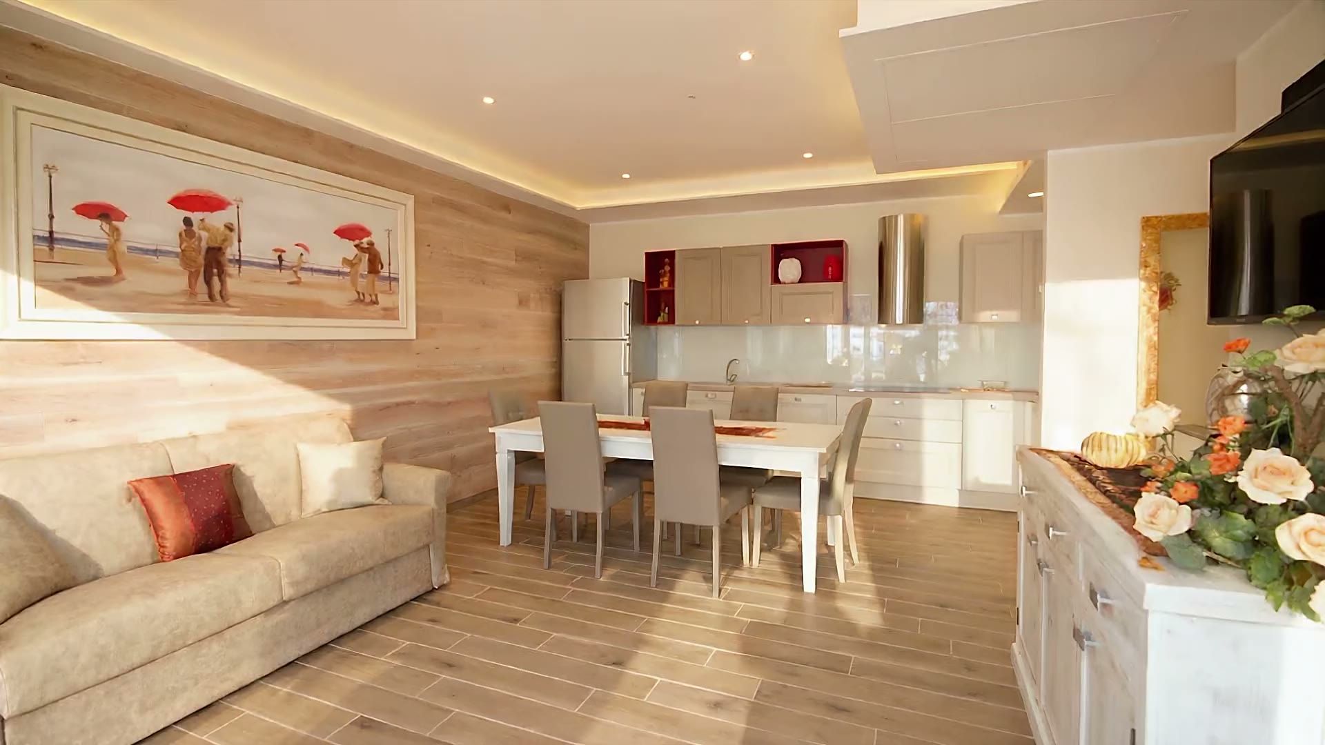 Il soggiorno di Casa Dune con la parete in legno e il quadro, il divano letto, il tavolo bianco da sei e la cucina attrezzata