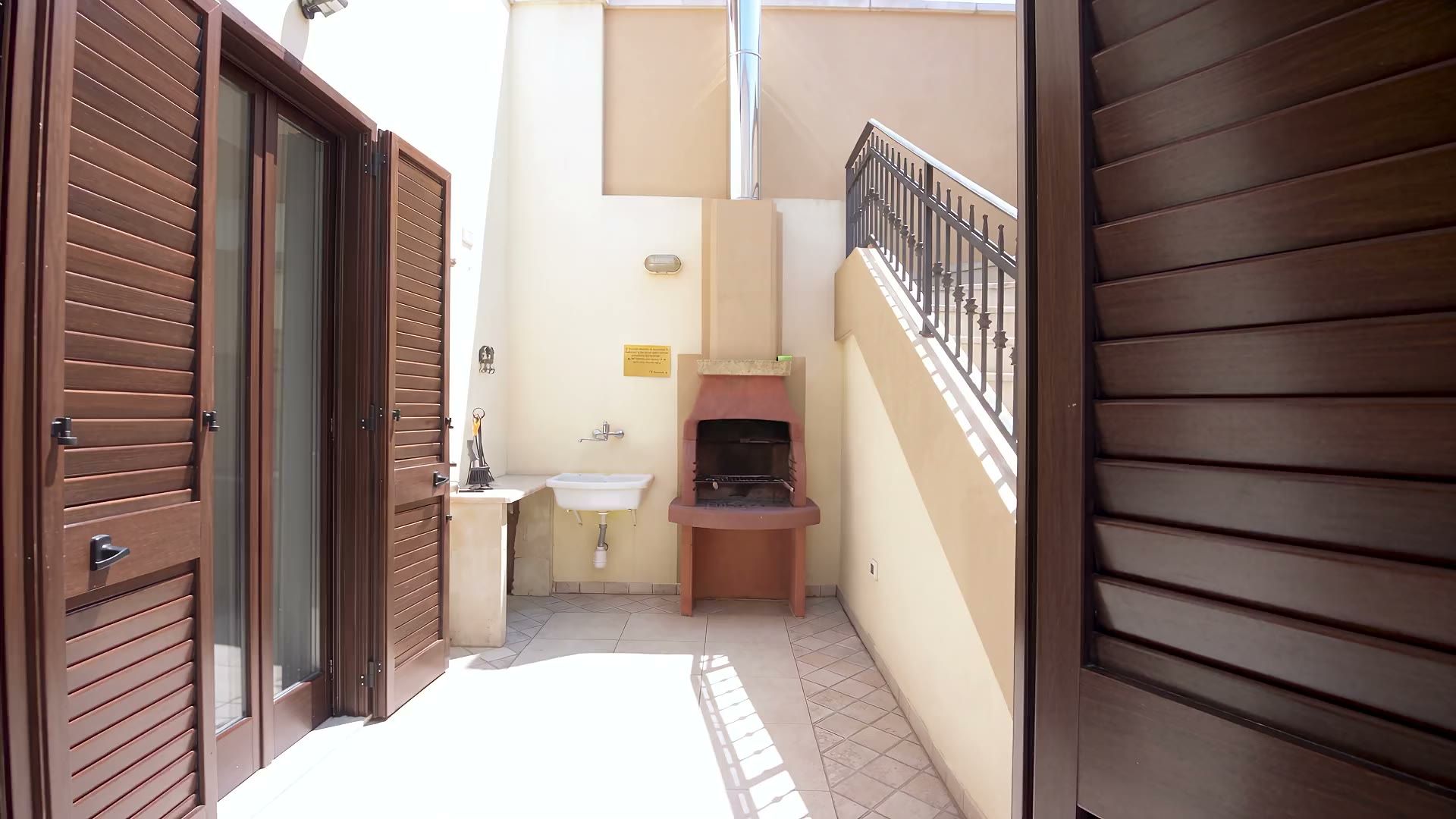 La corte del barbecue di Casa Pescoluse 9: il lavabo in pietra, il barbecue in muratura e la scala che sale al gazebo
