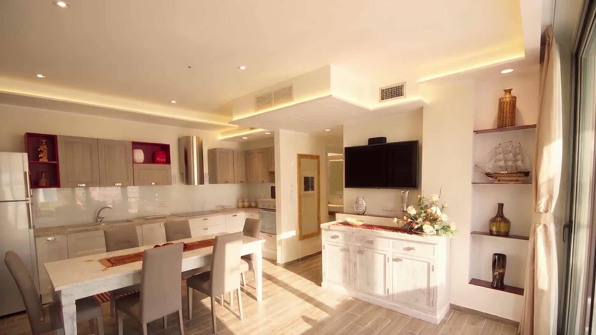 Il soggiorno di Casa Dune in un giro: il divano letto, il tavolo bianco da sei, la cucina con il piano a induzione, la credenza bianca e la TV