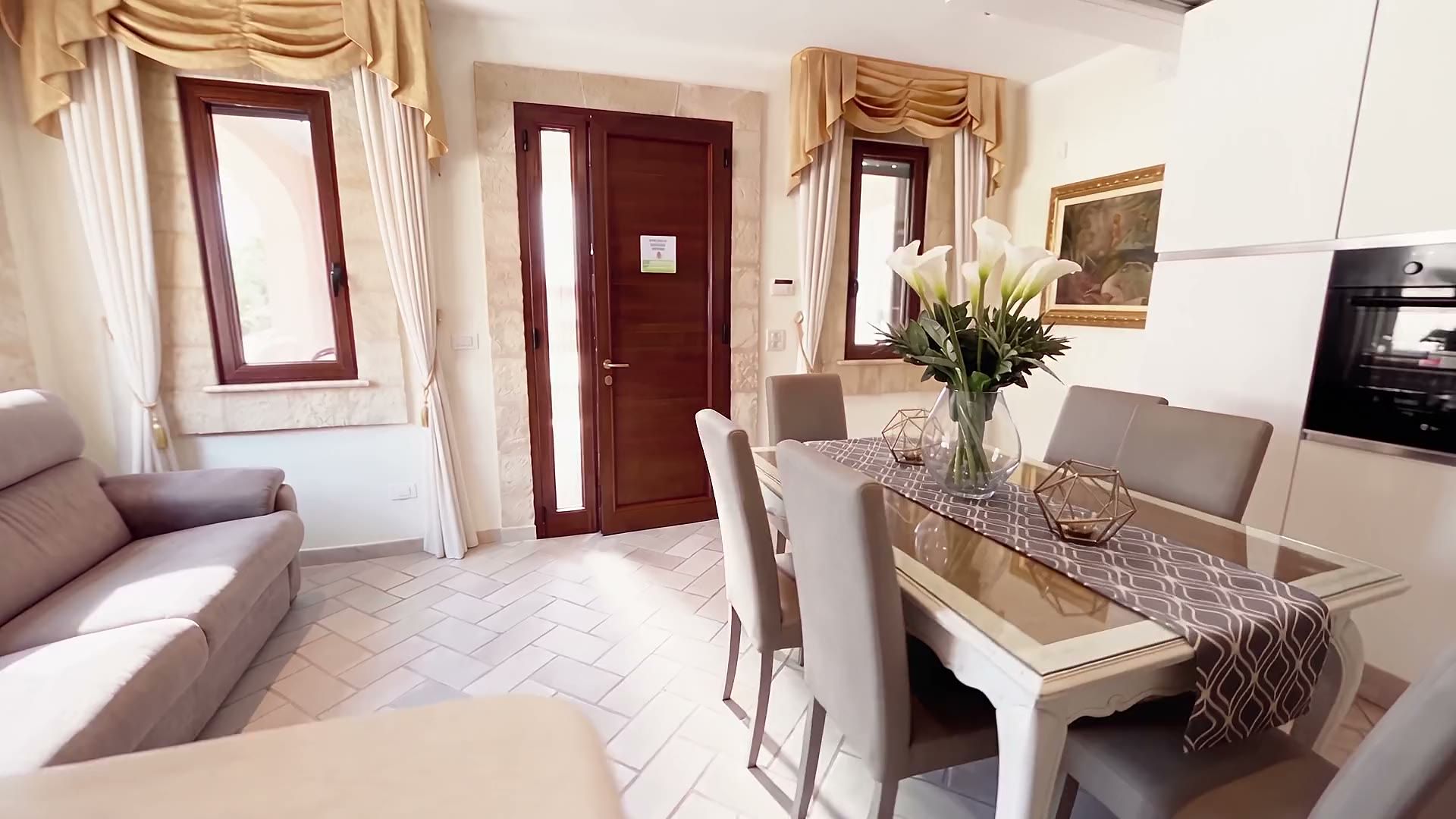 Il soggiorno di Casa Pescoluse 4: il divano letto, il tavolo da pranzo, le finestre con le tende dorate e l'arco in pietra verso le camere