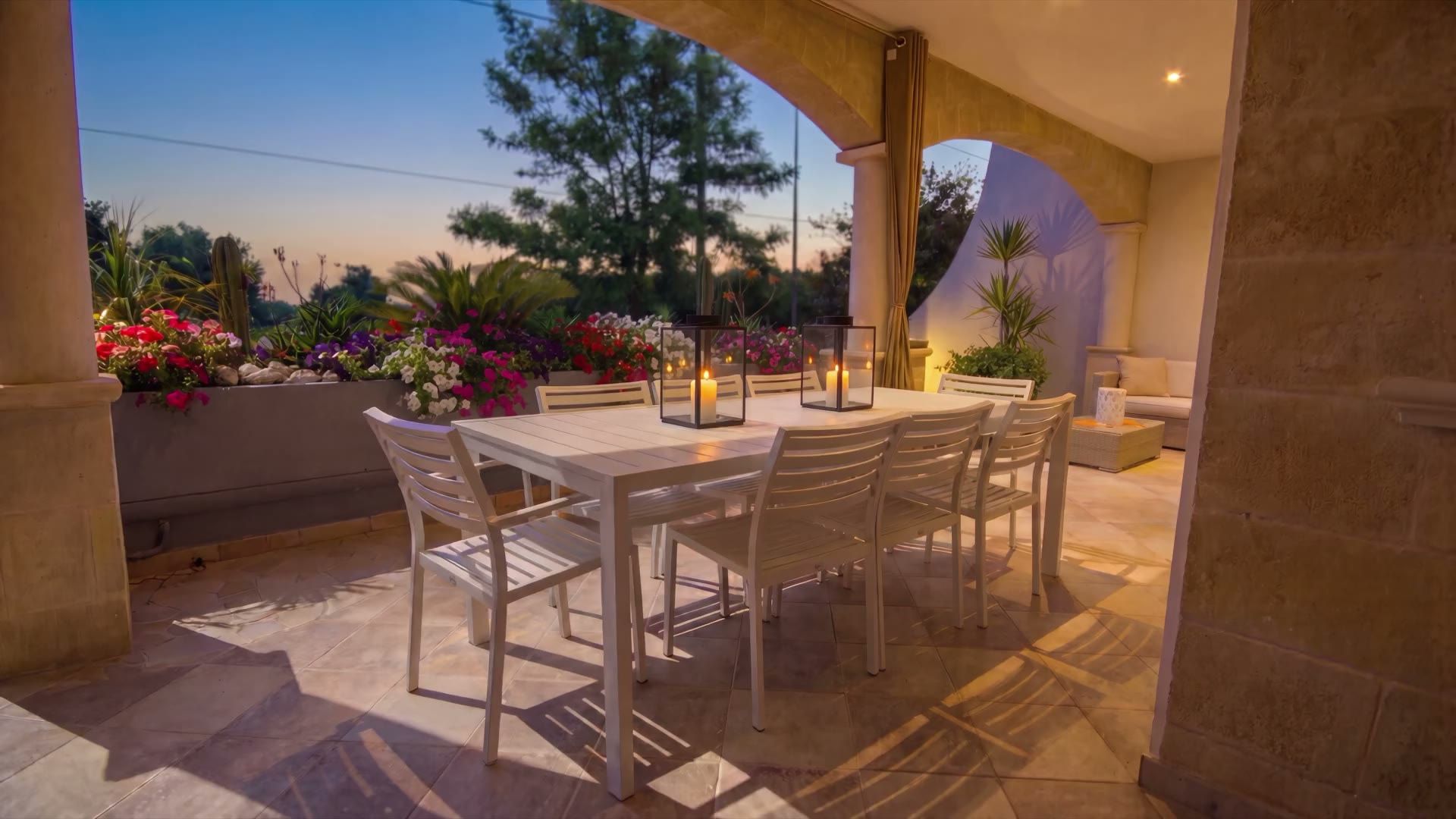 La veranda di Casa Pescoluse 1 al crepuscolo, con le candele accese sul tavolo da pranzo e le luci calde sotto gli archi