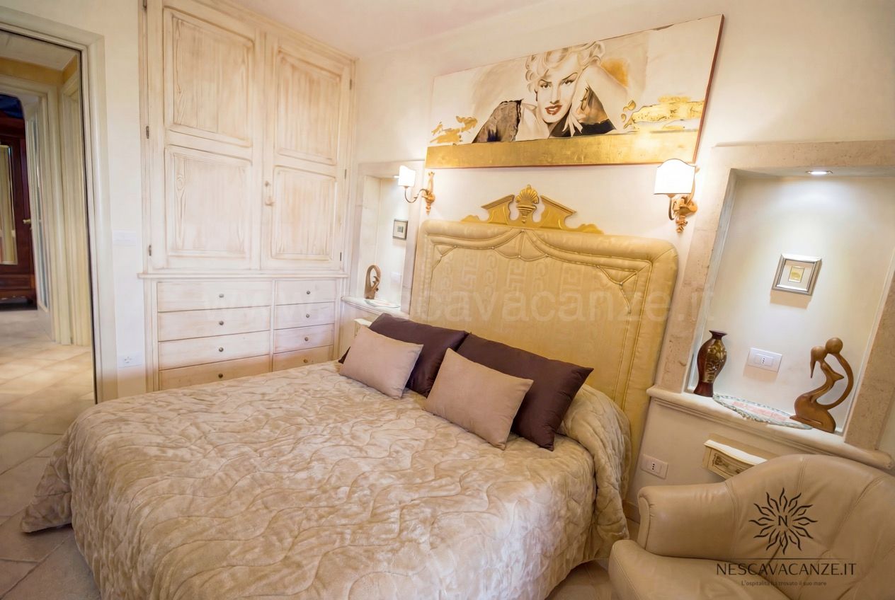 Casa Pescoluse 6 - camera matrimoniale con testiera dorata, quadro di Marilyn, armadio chiaro e poltrona
