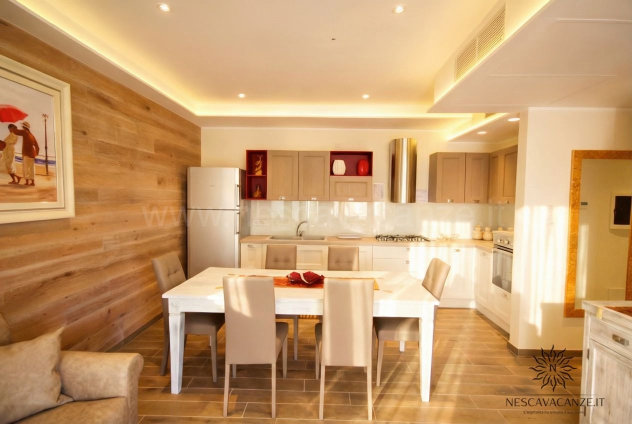 Casa Dune - sala da pranzo e cucina a vista con tavolo bianco, sedie beige e frigorifero