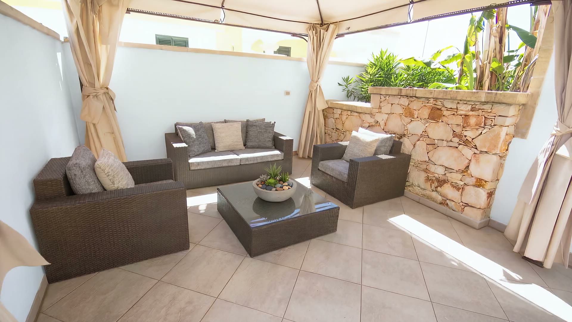 Il gazebo di Casa Pescoluse 9 con i divani in rattan, i cuscini chiari, i tendaggi e il muro a secco