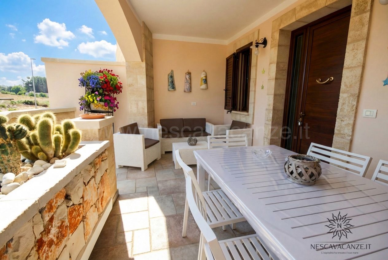 Casa Pescoluse 5 - veranda coperta con tavolo, divano in rattan, cactus e vista sul giardino