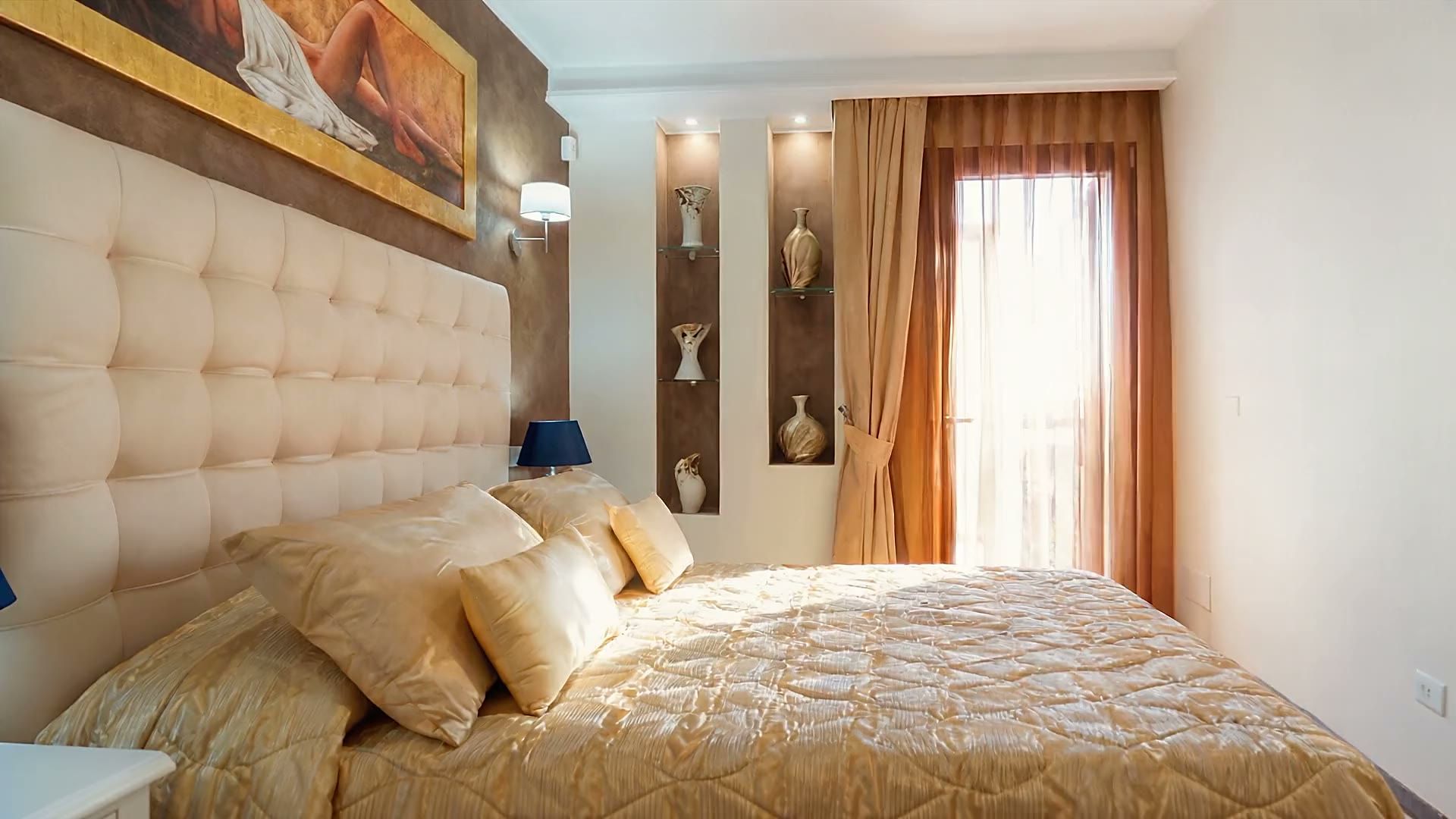 La prima camera matrimoniale di Casa Salento con il copriletto in raso dorato, la testiera imbottita, la parete bronzo con il quadro e la finestra