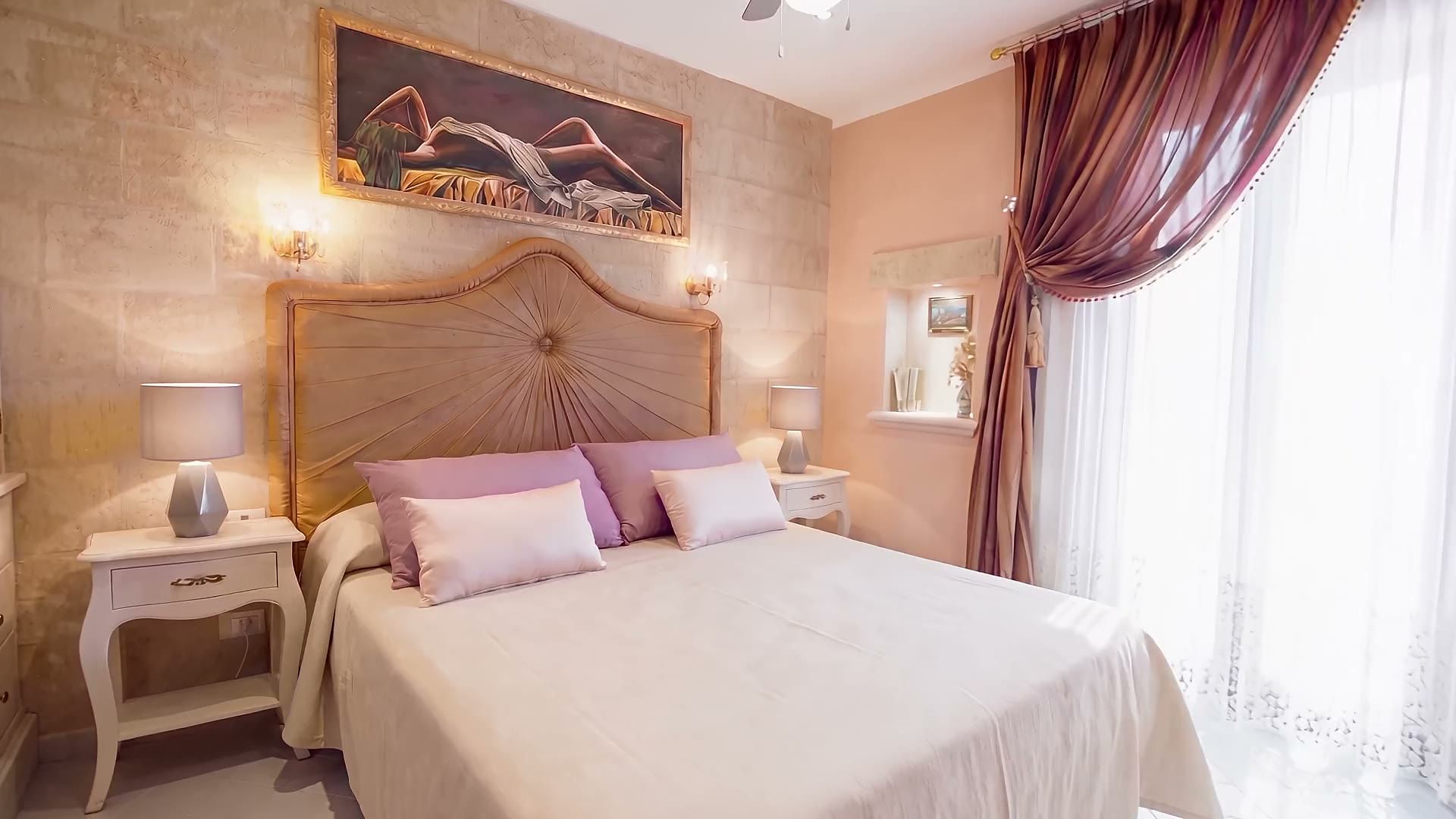 La camera matrimoniale di Casa Pescoluse 4 con la testiera imbottita dorata, la coperta beige, i comodini bianchi e il muro in tufo