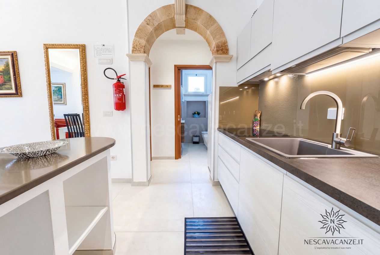 Casa Pescoluse 3 - cucina a corridoio con piano in pietra scura, lavello e arco in tufo verso il bagno