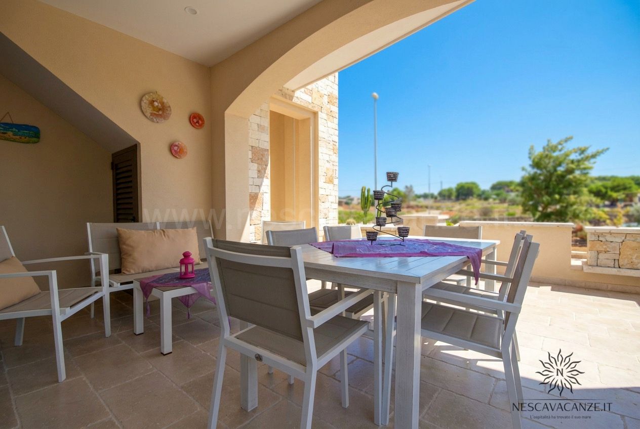 Casa Giglio - patio coperto con tavolo bianco, poltrone e vista sulla campagna sotto cielo azzurro
