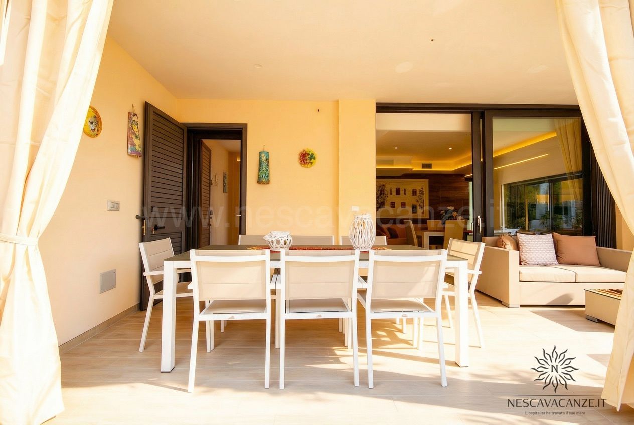 Casa Salento - veranda con tavolo da pranzo per otto, sedie bianche e divano affacciata sul soggiorno