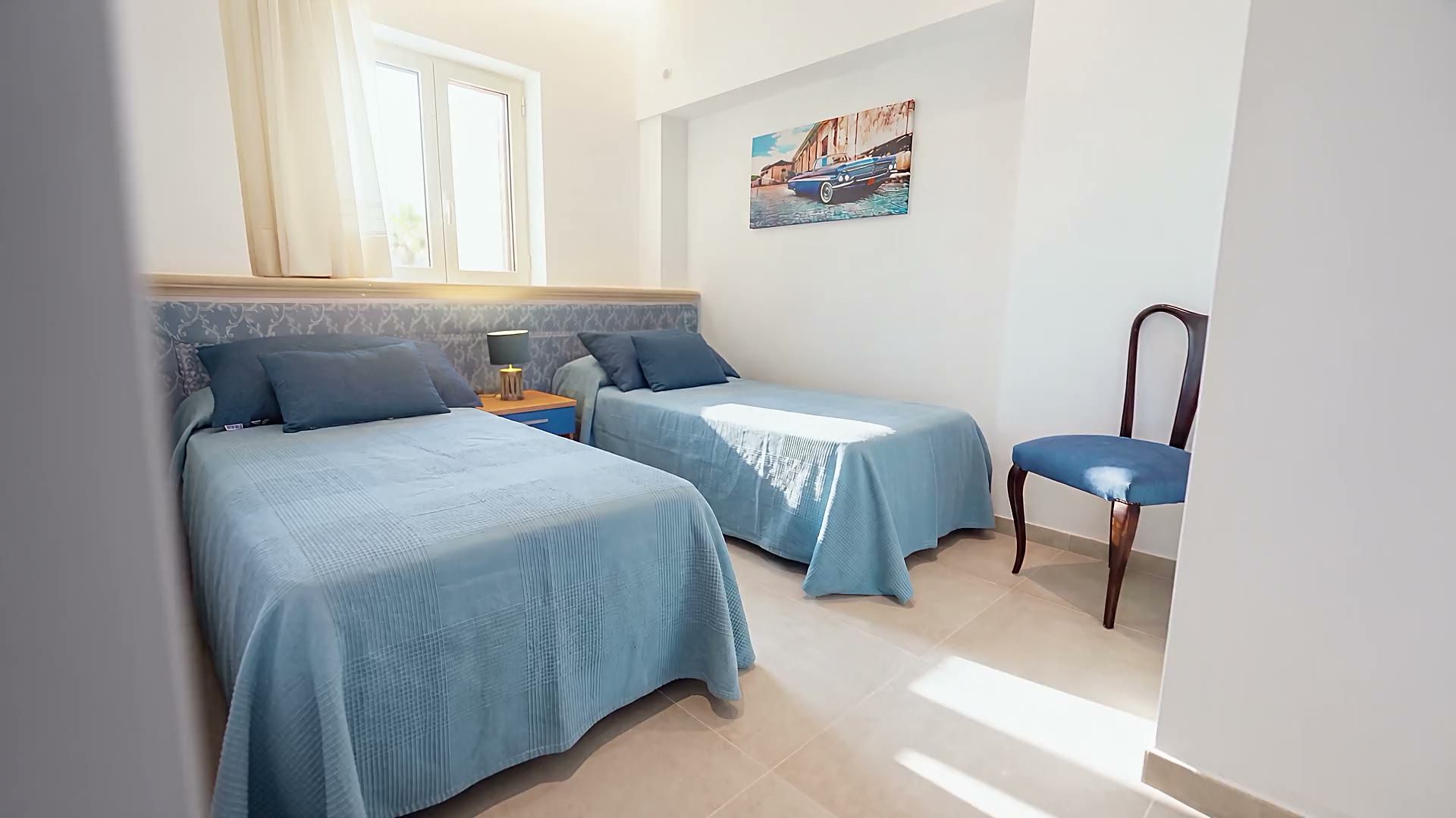 La camera azzurra di Casa Pescoluse 2 con i due letti singoli, la sedia blu e la finestra