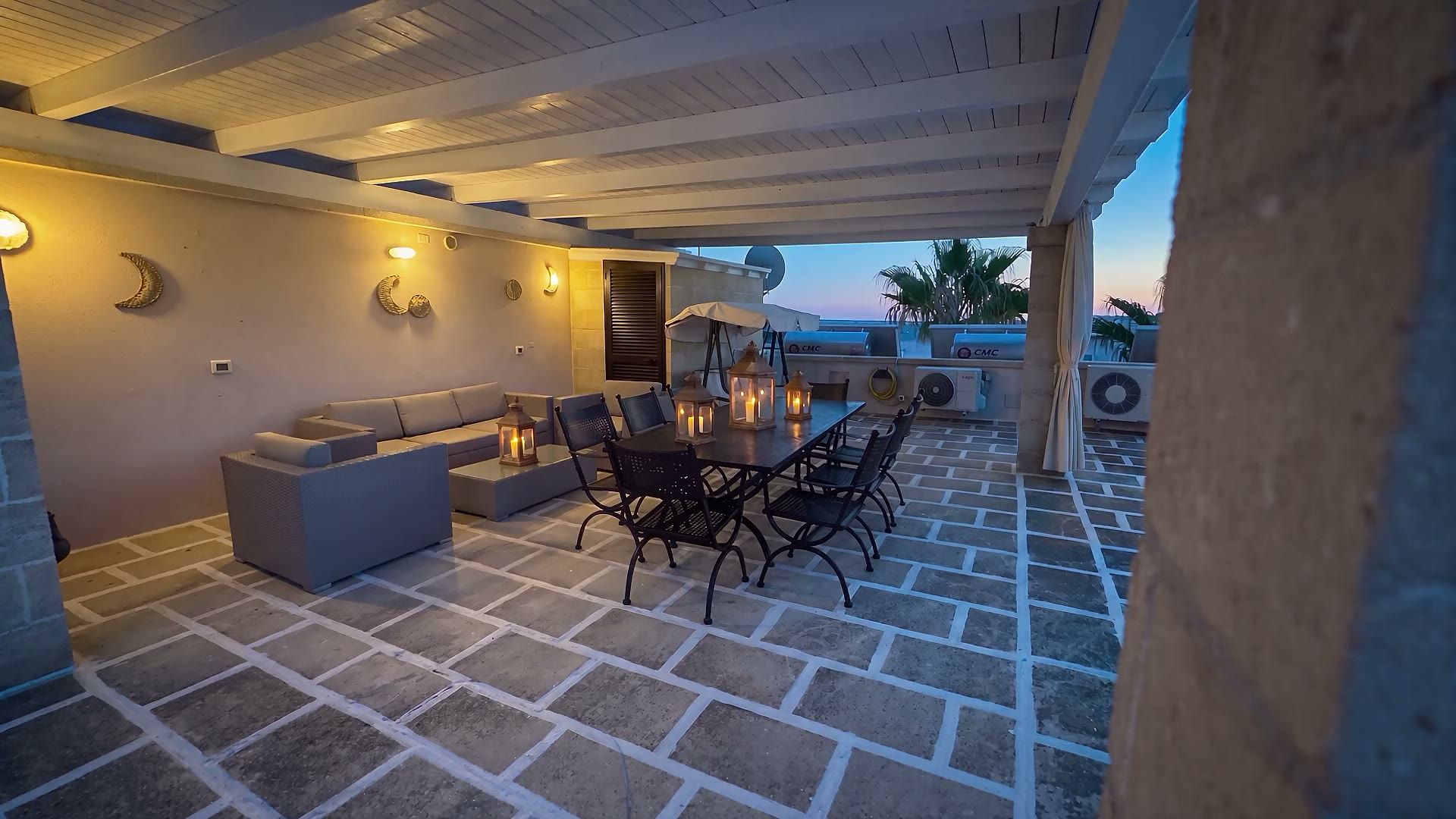 La tettoia del terrazzo di Casa Pescoluse 4 la sera, con le luci accese sul tavolo e il cielo blu dell'imbrunire