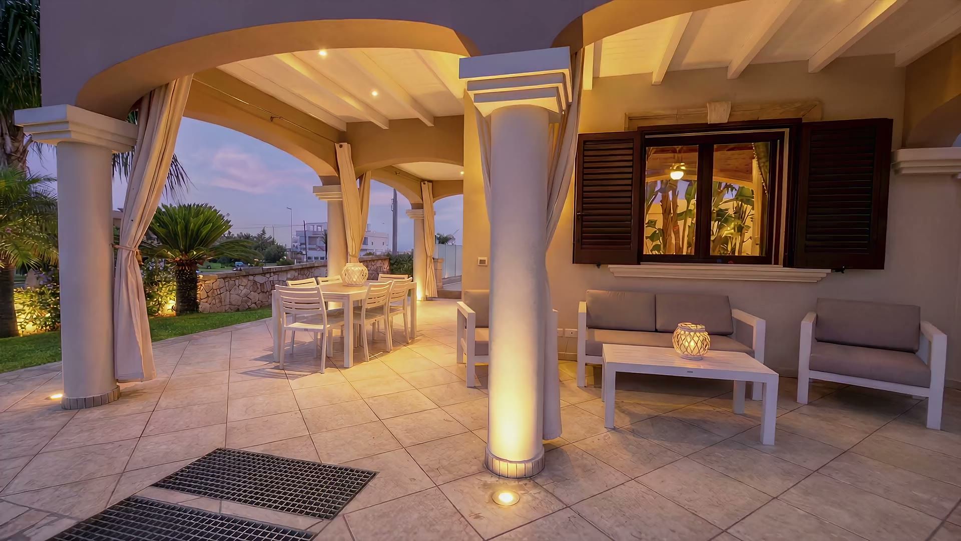 Casa Pescoluse 8 al tramonto: il porticato illuminato, le lanterne sui gradini e le sfere luminose sul prato