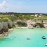 Acqua turchese e barche nella baia sotto la scogliera