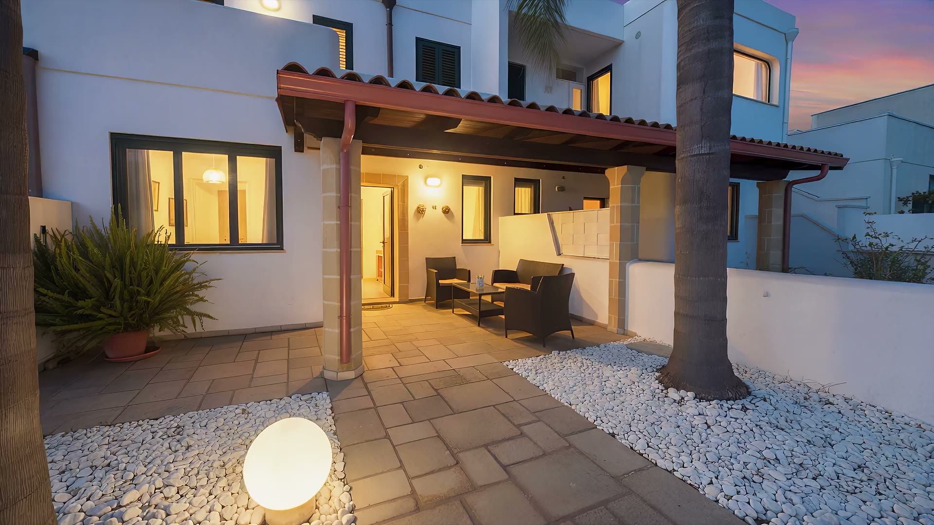 Casa Sabbia d'Oro la sera: la veranda illuminata, il cancello nero e le palme sotto il cielo blu dell'imbrunire