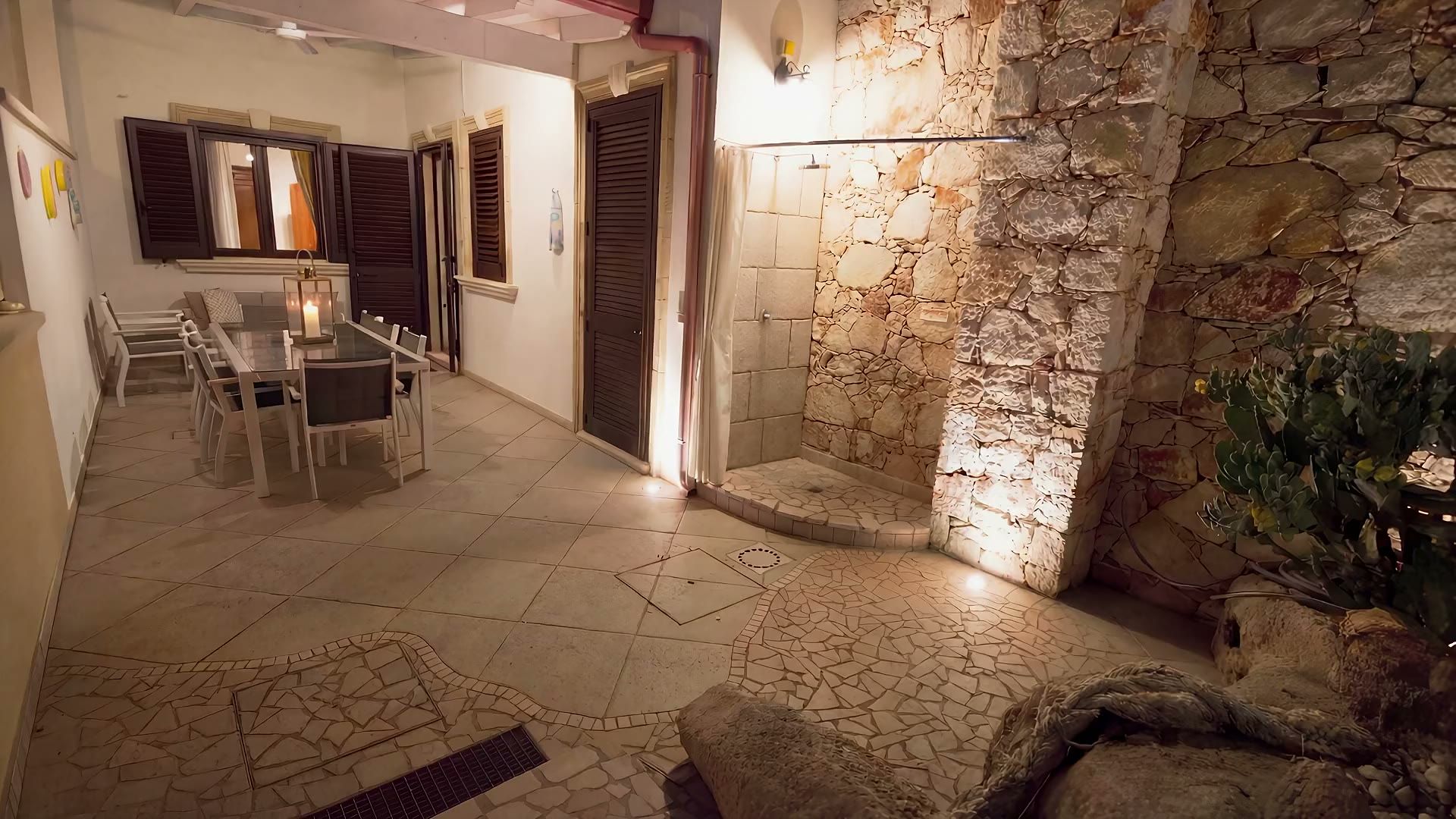 La veranda di Casa Pescoluse 9 la sera: le lanterne accese sul tavolo, la doccia in pietra illuminata e i faretti nel vialetto