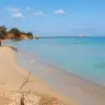 Lunga spiaggia di sabbia ad Apani con il faraglione rosso e il mare calmo