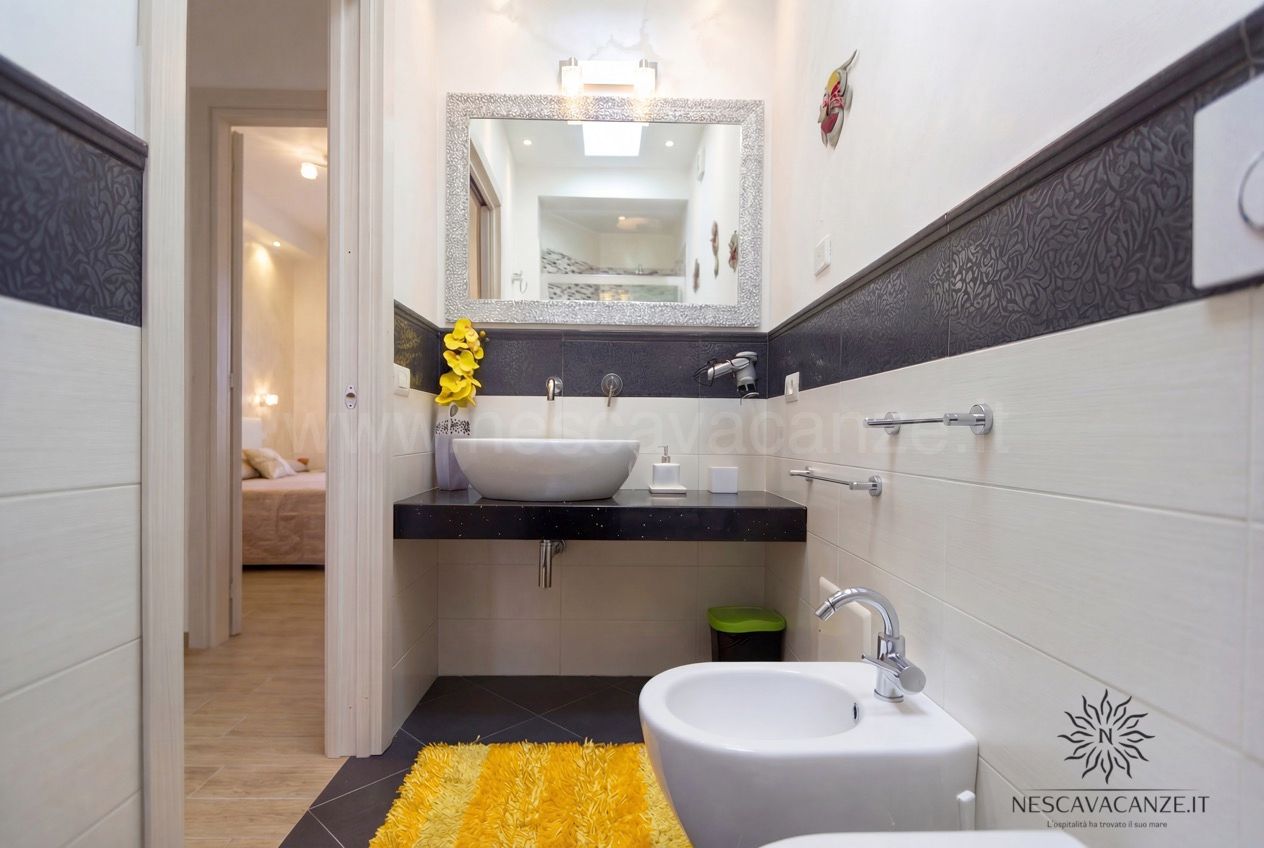 Casa Giglio - bagno con lavabo ovale, specchio argentato, bidet e tappeto giallo