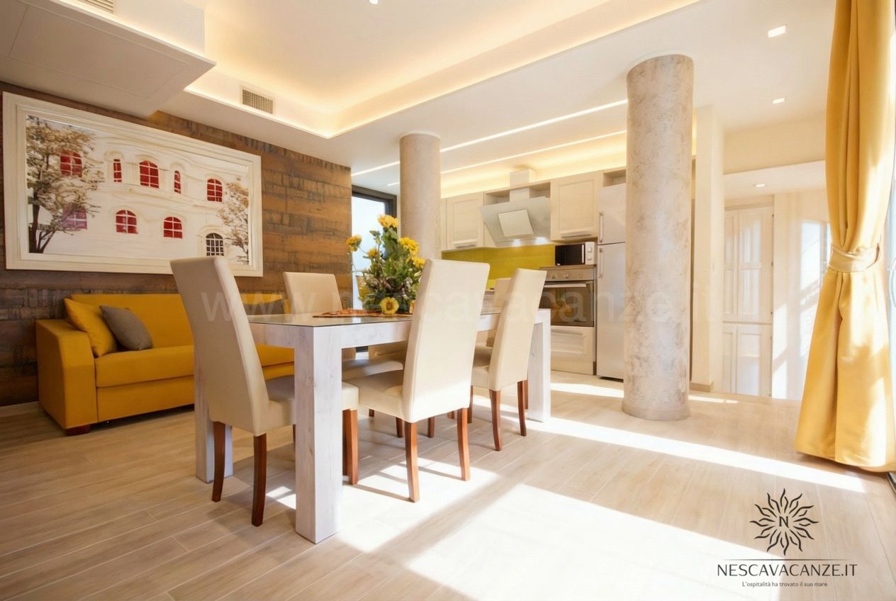 Casa Salento - soggiorno con tavolo da pranzo, divano giallo, angolo cottura e colonne in marmo