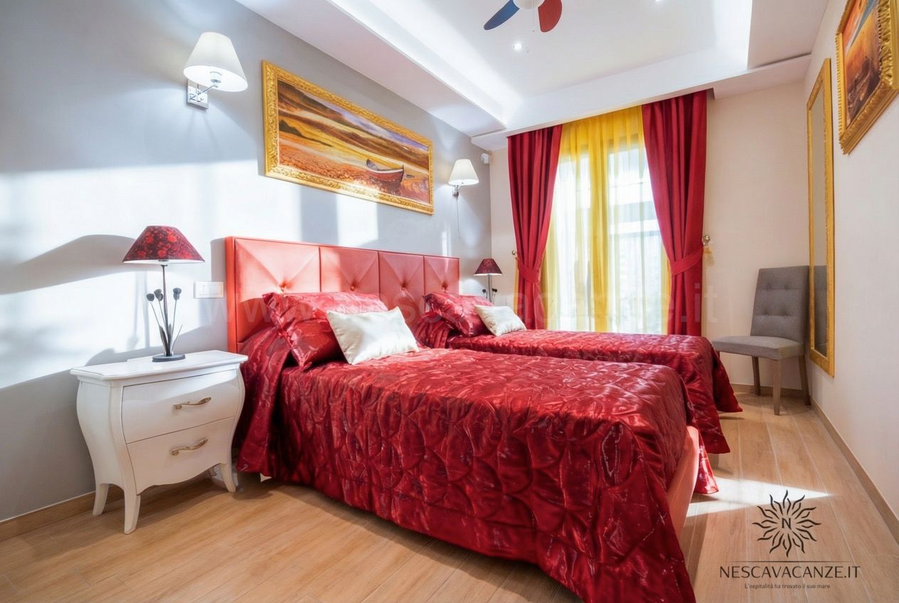 Casa Salento - camera con due letti singoli e copriletto rosso, comodino bianco e quadro di una barca