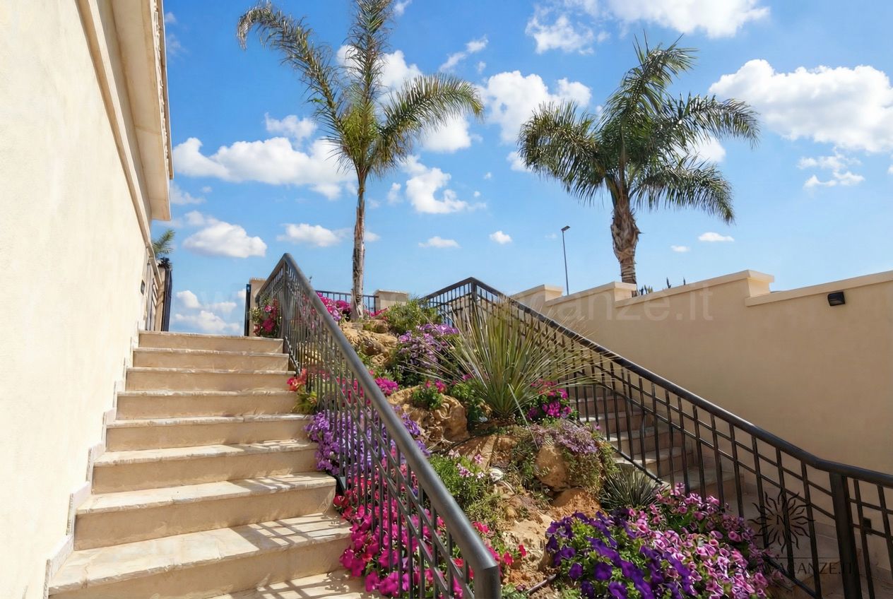 Casa Salento - scala esterna in pietra fiancheggiata da petunie fiorite e palme sotto cielo azzurro