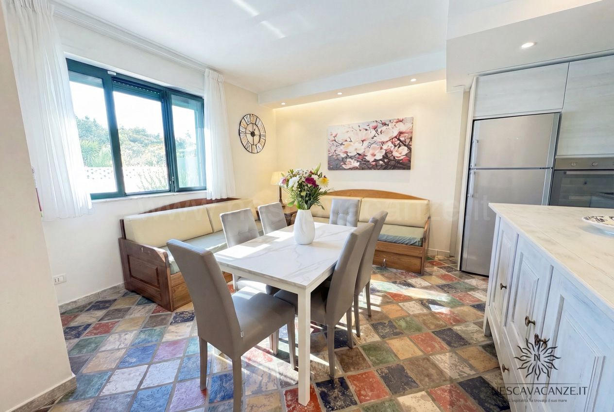 Casa Sabbia Oro - zona pranzo con tavolo e sei sedie, divani, finestra e quadro floreale