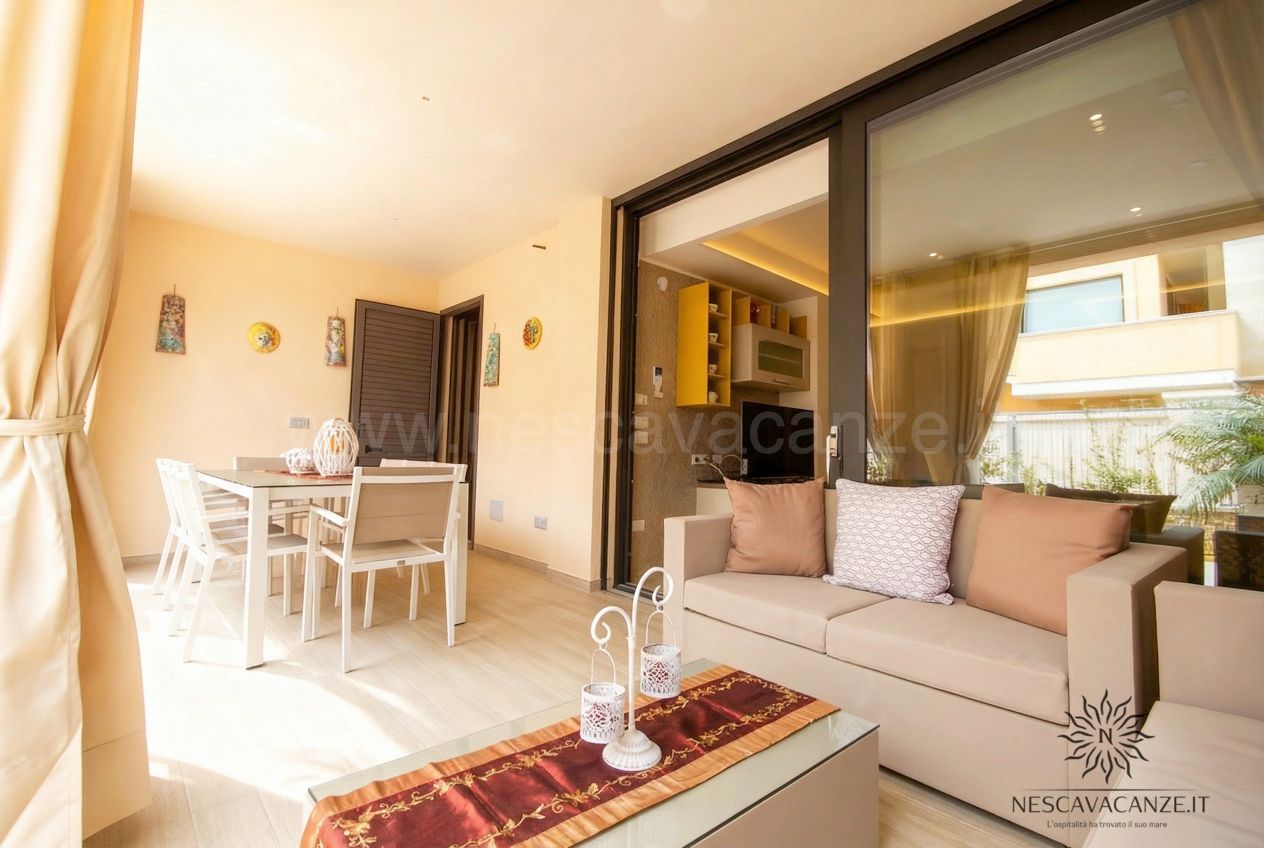 Casa Salento - veranda coperta con divano beige, tavolo bianco e angolo cottura con paraschizzi giallo