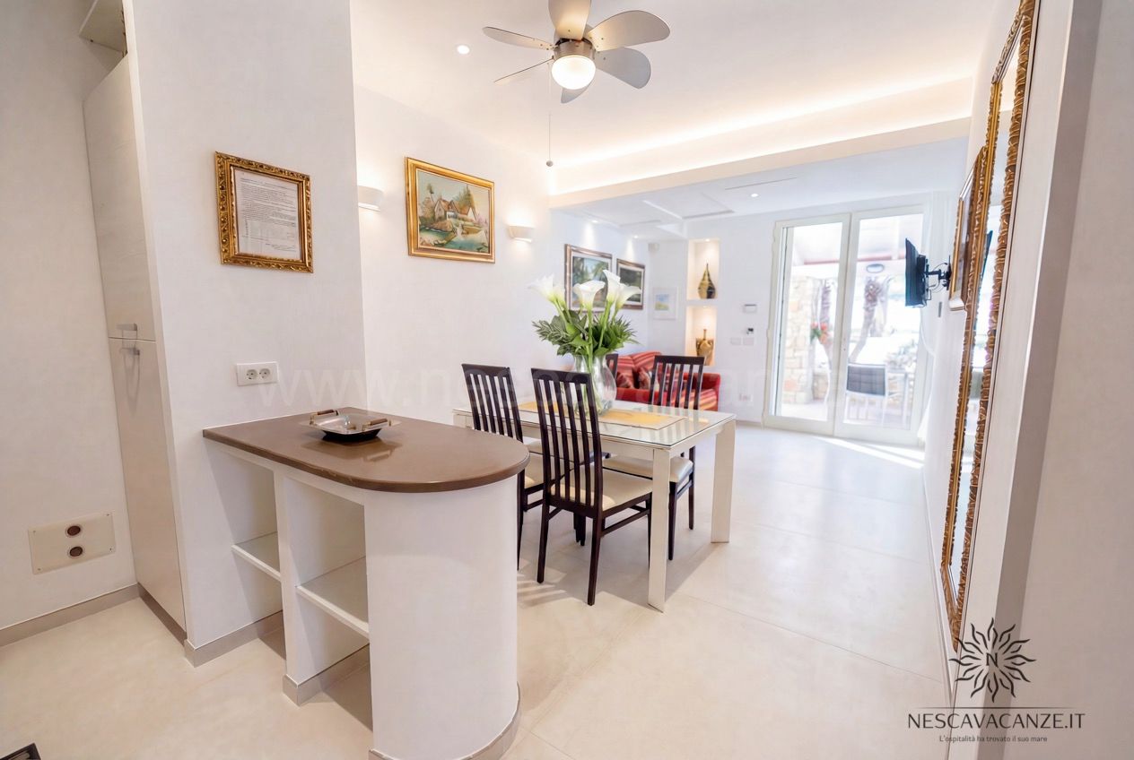 Casa Pescoluse 3 - zona pranzo con tavolo in vetro, ventilatore a soffitto e divano rosso affacciata sulla veranda