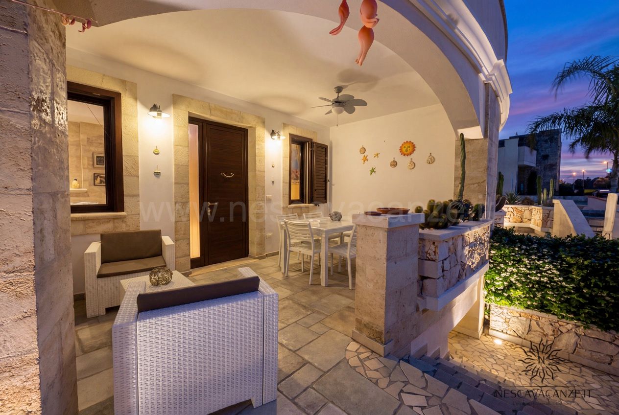 Casa Pescoluse 5 - portico al tramonto con porta d'ingresso, tavolo e divano in rattan